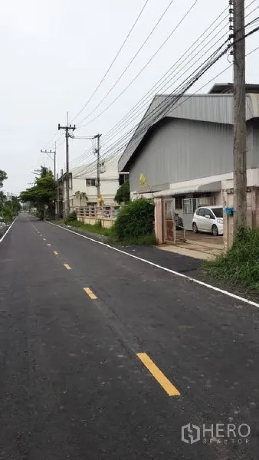 工厂 出租在Lat Lum Kaeo, Pathum Thani - 双车道柏油路与金属板工厂外立面，旁有电线与停车位。