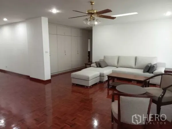 Condominium for rent in Watthana, Bangkok - Spacious living room with L-shaped sofa, parquet floors, ceiling fan and built-in storage.