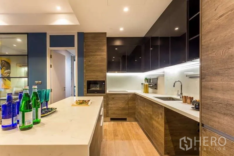 Condominium for rent in Pathum Wan, Bangkok - U-shaped kitchen with wood cabinetry, stone countertops and island.
