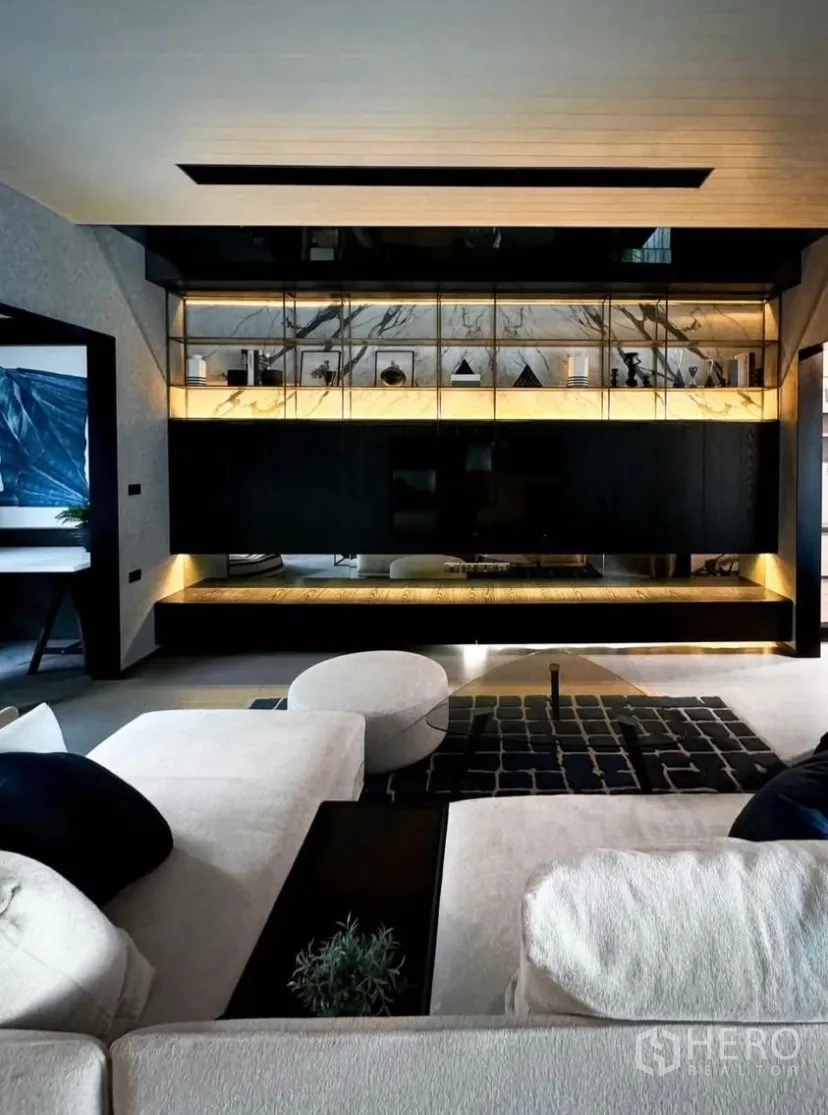 Townhouse for rent or sale in Bang Phli, Samut Prakan - Stylish living room featuring illuminated marble shelving, dark cabinetry and a low sectional sofa.