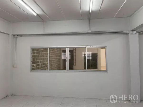 Warehouse for rent in Min Buri, Bangkok - Bright tiled office room with sliding windows overlooking the warehouse floor.
