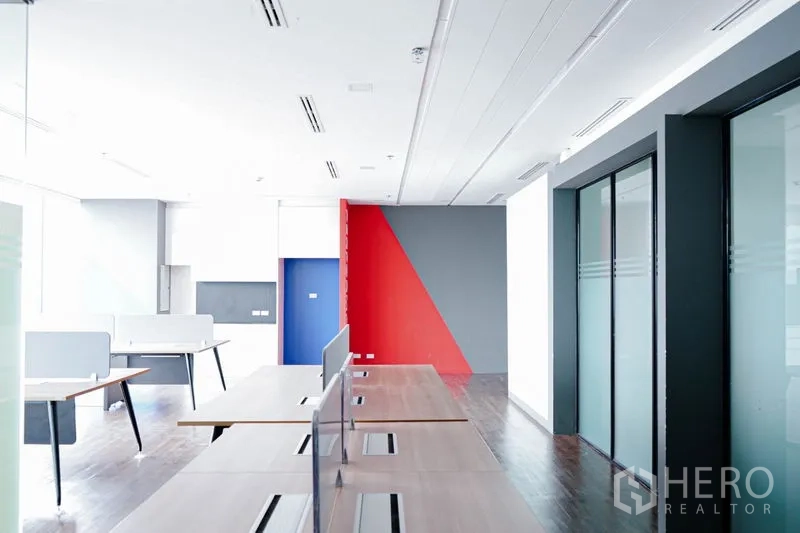 Office Space for rent in Khlong Toei, Bangkok - Modern office area with long workstation benches, ceiling air vents, and bold red and blue accent walls.