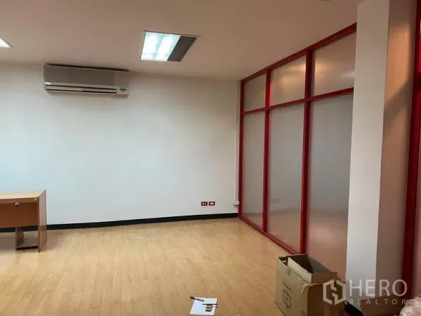 Office Space for rent in Khlong Toei, Bangkok - Private office area featuring a red-framed frosted glass partition, wall-mounted air conditioner, light wood flooring and a desk.