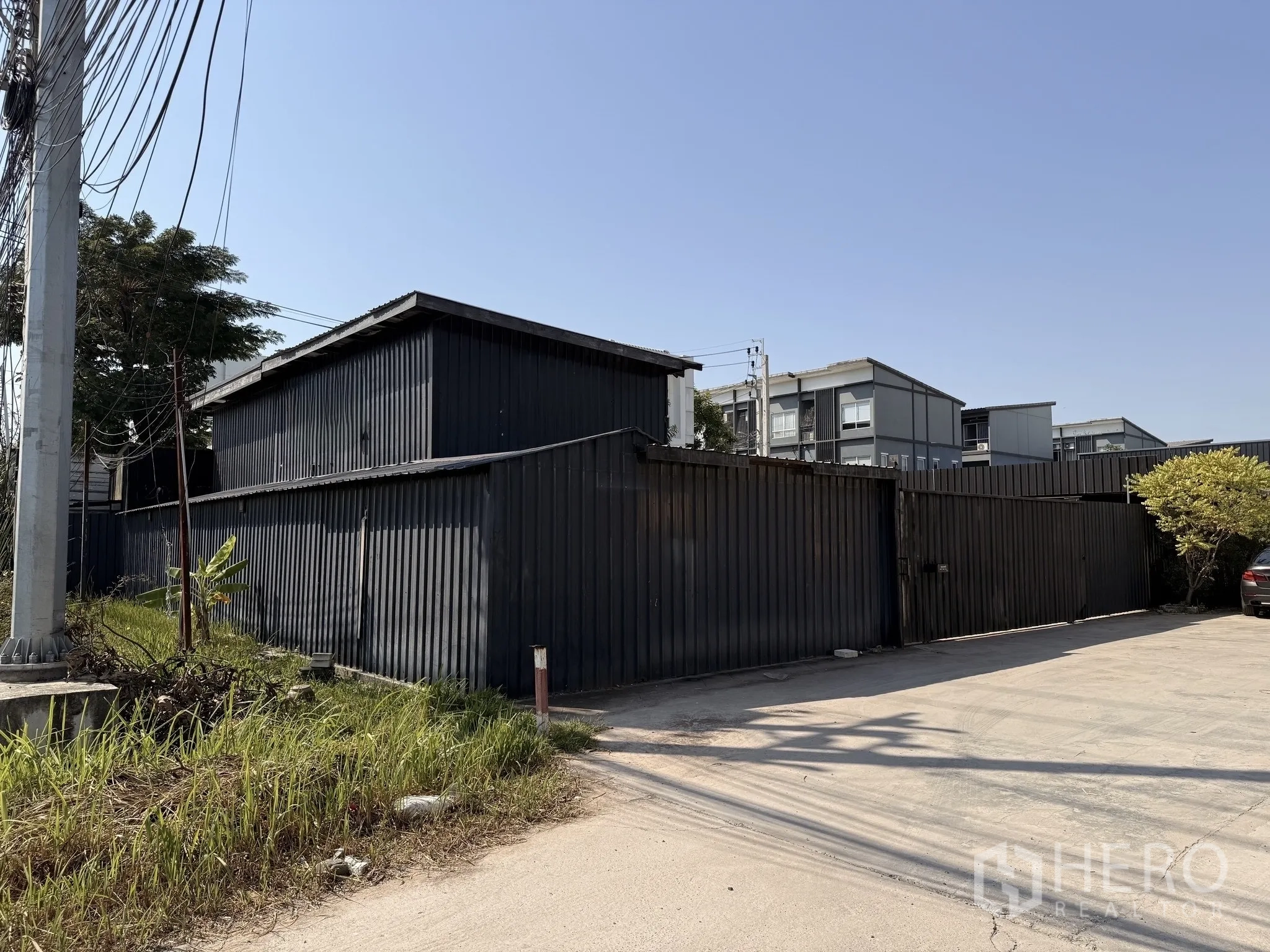 货栈 for rent in Lat Krabang, Bangkok - 曼谷Prawet区黑色金属围挡的仓库外立面与宽阔出入口的街景。