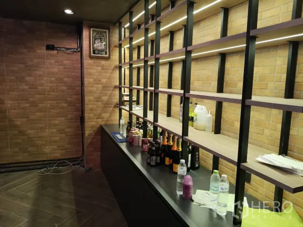 Retail Space for rent - Back‑bar wall with illuminated shelving and brick backdrop for bottle display.