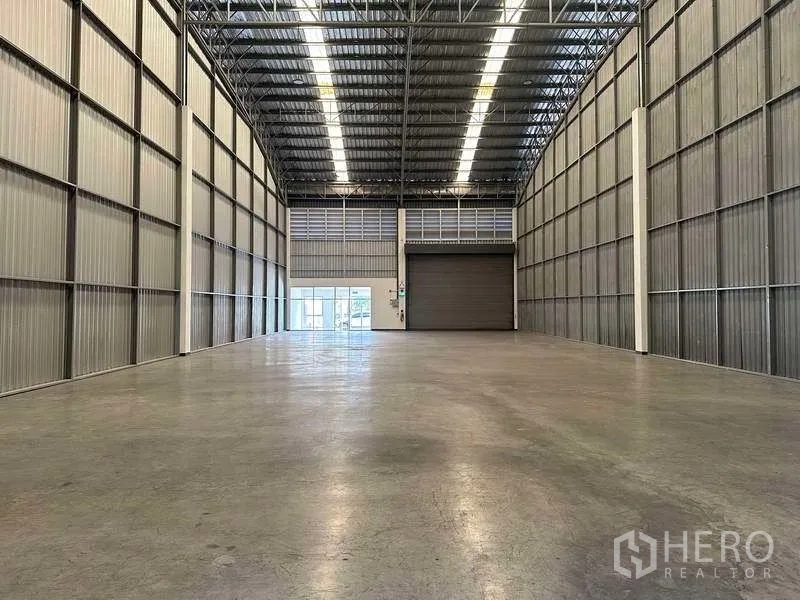 Factory for rent in Bang Sao Thong, Samut Prakan - Warehouse view toward a roller shutter and adjoining glass office area.