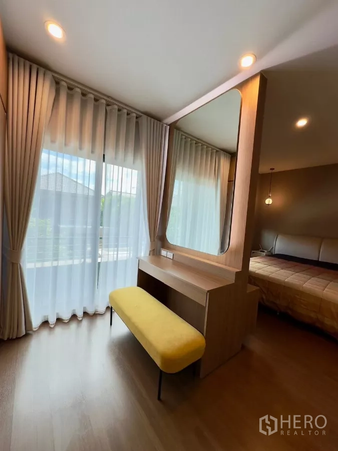 独立式住宅 出租在Samut Prakan - 梳妆台带大镜与长凳，旁为通往阳台的纱帘。