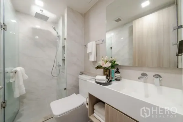 คอนโด ขายในWatthana, Bangkok - ห้องน้ำสมัยใหม่พร้อมตู้ฝักบัวกระจก เรนชาวเวอร์ อ่างล้างหน้าแผงยาว กระจกบานใหญ่ และผนังลายหินอ่อนโทนอ่อน