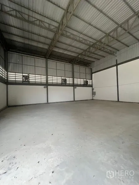 Warehouse for rent or sale in Sai Noi, Nonthaburi - Empty warehouse interior with high steel truss ceiling and smooth concrete floor.