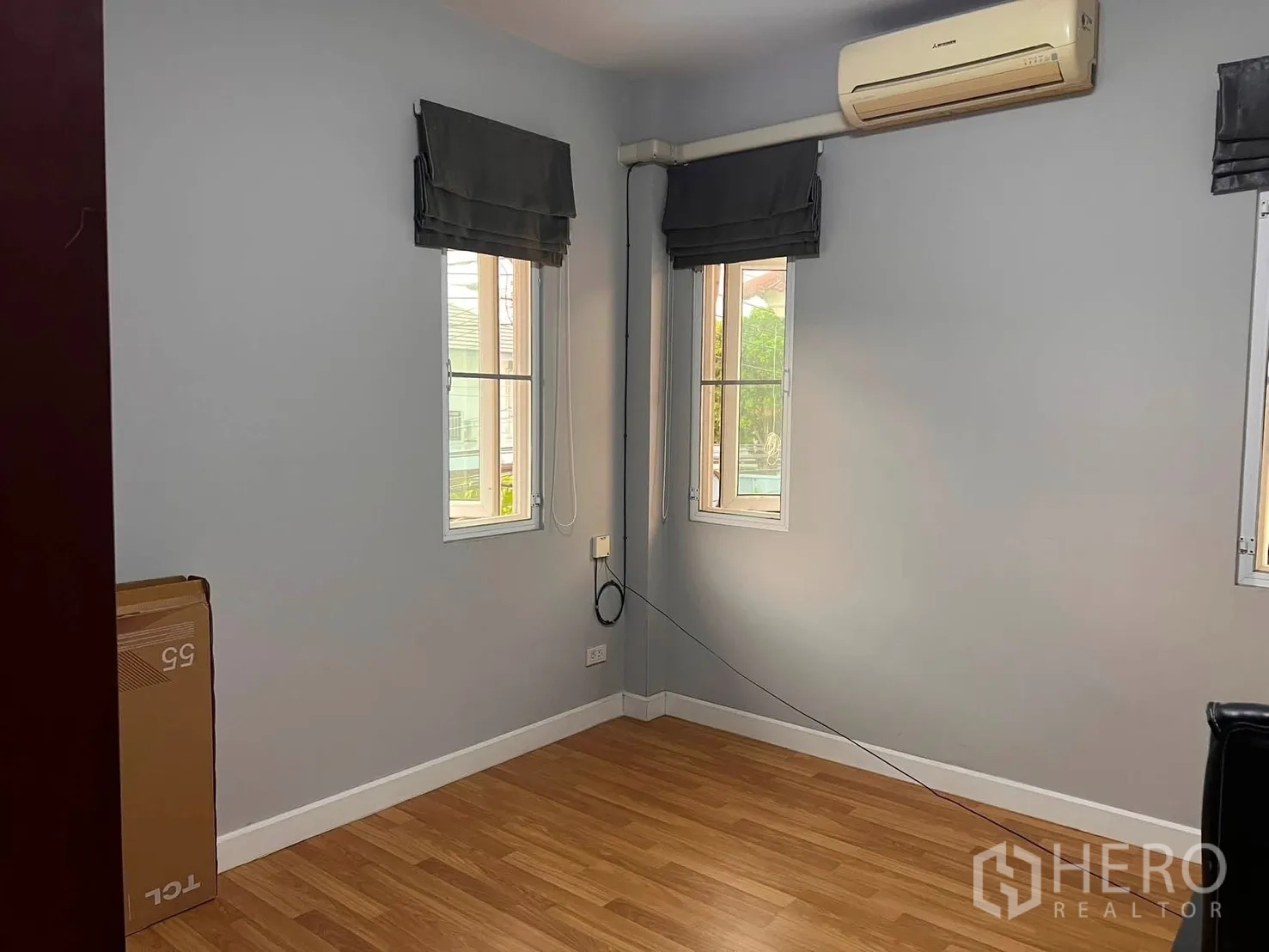 Detached House for rent in Watthana, Bangkok - Empty gray-walled room with wood floor, three windows, and an air conditioner.