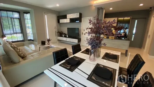 Detached House for rent in Samut Prakan - Open-plan living and dining area with TV wall unit and set dining table.