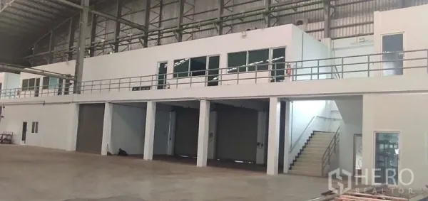 Warehouse for rent in Nong Chok, Bangkok - Mezzanine office with glass windows above multiple roller-shutter bays inside the warehouse.