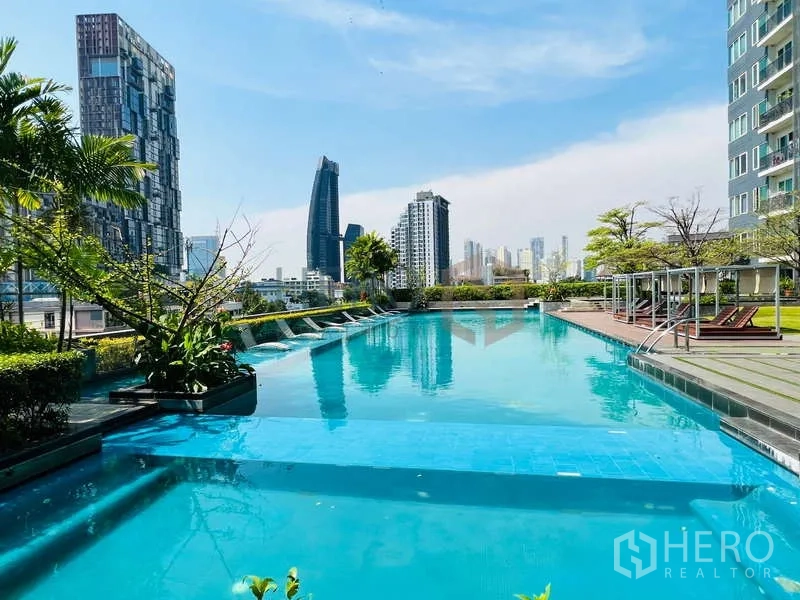 Condominium for sale in Khlong Toei, Bangkok - Rooftop swimming pool with city skyline views and sun loungers.