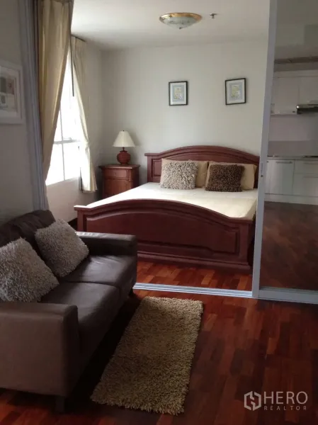 Condominium for rent in Pathum Wan, Bangkok - Cozy bedroom with wooden bed, sofa seating and large window over warm wood floors.