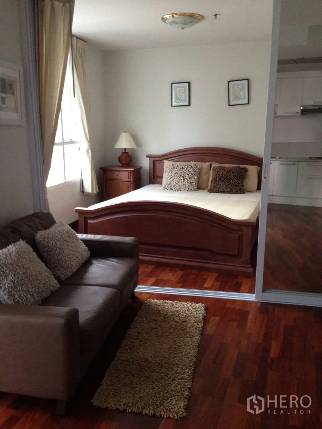 Condominium for rent in Pathum Wan, Bangkok - Cozy bedroom with wooden bed, sofa seating and large window over warm wood floors.