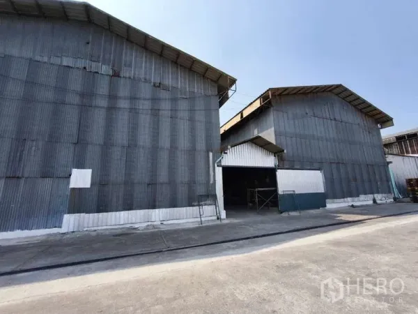 Warehouse for rent in Krathum Baen, Samut Sakhon - Exterior of corrugated steel warehouse buildings with high gable roofs and a wide driveway in Krathum Baen, Samut Sakhon.