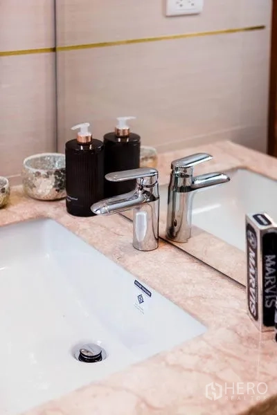 Condominium for rent in Huai Khwang, Bangkok - Close-up of bathroom vanity with marble countertop, chrome faucet, mirror and toiletries.