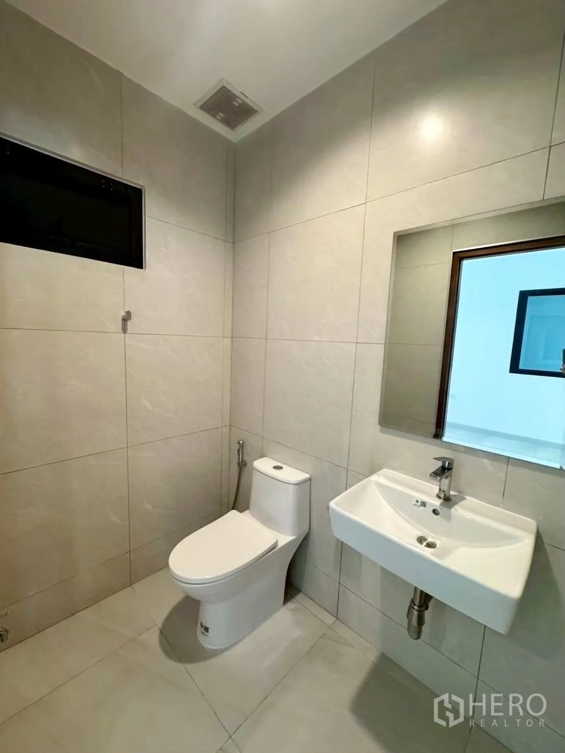 Home Office for rent in Wang Thonglang, Bangkok - Tiled bathroom with wall-mounted sink, mirror, toilet, and small window.