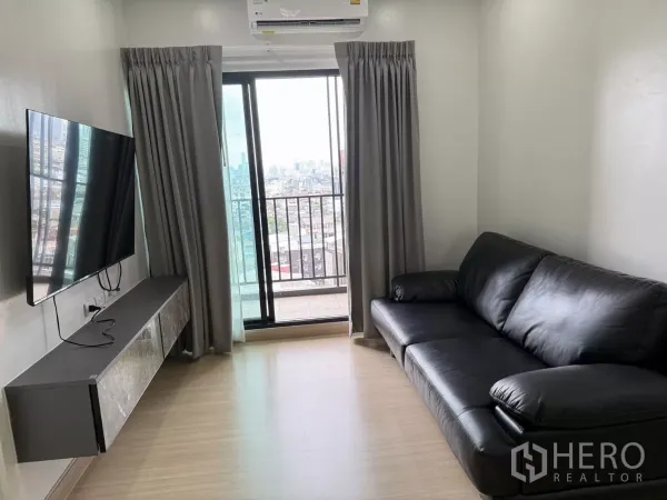 คอนโด ให้เช่าในKhlong Toei, Bangkok - ห้องนั่งเล่นสว่าง โซฟาหนังสีดำ ทีวีติดผนัง และประตูกระจกออกสู่ระเบียงวิวเมือง