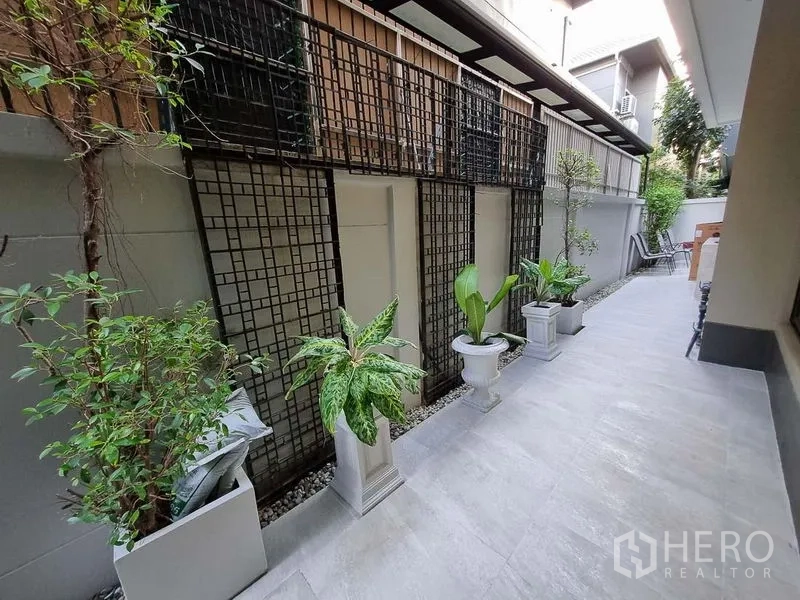 Detached House for rent in Bang Khae, Bangkok - Side courtyard with tiled walkway, decorative trellis, and potted greenery along the wall.