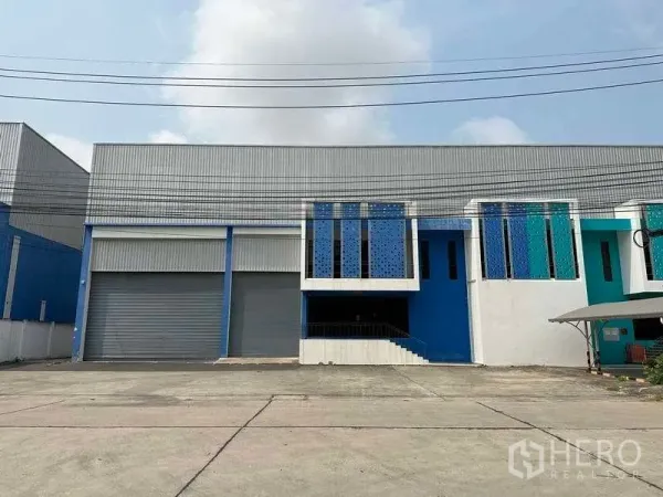 工厂 出租或出售在Bang Phli, Samut Prakan - 蓝白配色的工厂外立面，双宽幅卷帘门与宽阔混凝土前场。
