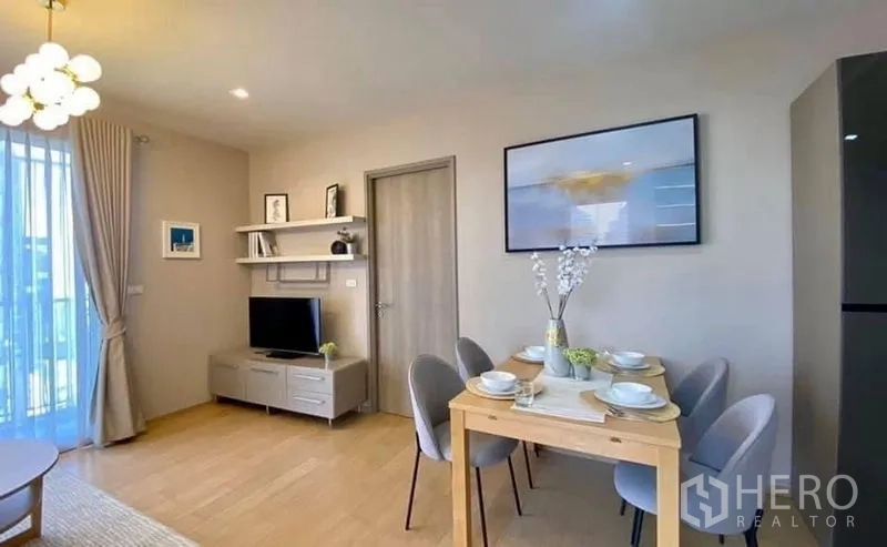 Condominium for rent or sale in Watthana, Bangkok - Cozy dining corner for four next to a media wall and shelves in a neutral-tone living space.