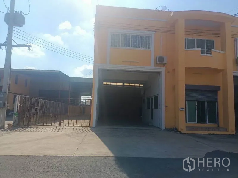 คลังสินค้า ให้เช่าในPathum Thani - ด้านหน้าโกดังสีเหลือง ติดถนน ประตูม้วนกว้าง พร้อมทางเข้ารั้วและลานจอด.