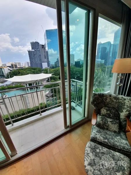 คอนโด ให้เช่าในChatuchak, Bangkok - มุมใกล้ระเบียงและประตูกระจกข้างเก้าอี้ มองเห็นสระว่ายน้ำ พื้นที่สีเขียว และเส้นขอบฟ้า