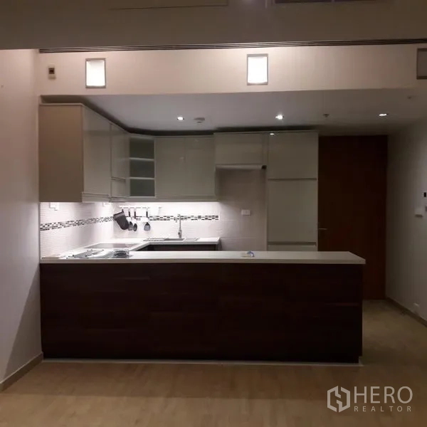 Condominium for sale in Sathon, Bangkok - Modern open‑plan kitchen with peninsula counter, glossy cabinets and under‑cabinet lighting.