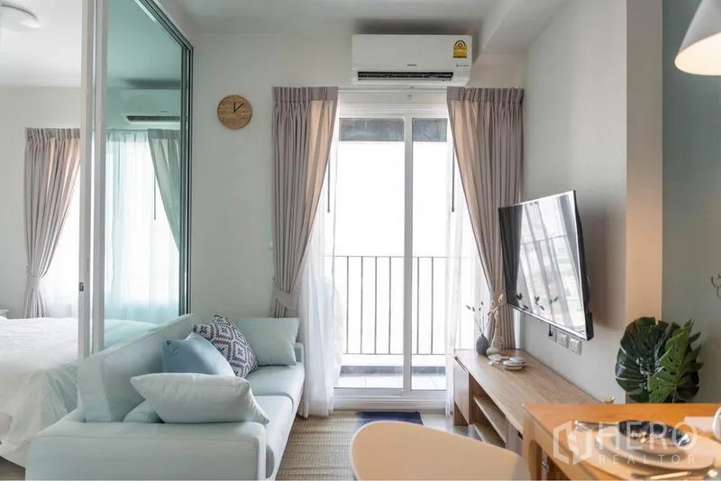 Condominium for sale in Huai Khwang, Bangkok - Open-plan lounge with pastel sofa facing a wall-mounted TV and a glass door leading to the balcony.