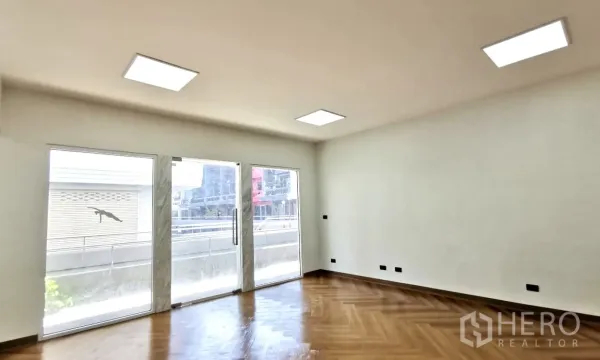 Home Office for rent in Watthana, Bangkok - Sunlit workspace with twin sliding glass doors opening to a balcony and warm wood flooring.