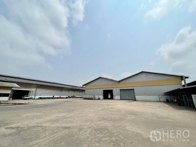 Warehouse for rent in Phra Samut Chedi, Samut Prakan - Expansive loading yard in front of twin-gable warehouses and parking space.