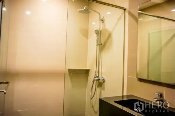 Condominium for sale in Watthana, Bangkok - Modern bathroom with glass-enclosed shower, rain shower head and vanity.