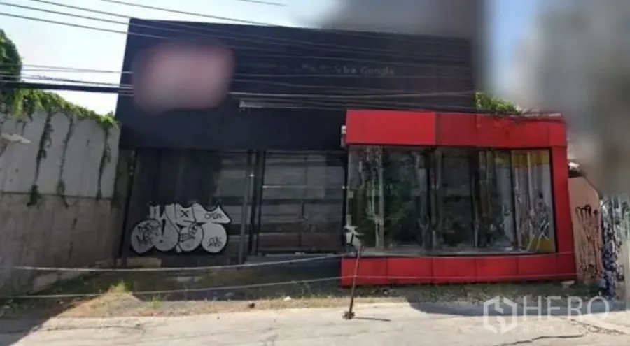 独立商业地产 出售在Watthana, Bangkok - 街景：黑色立面与红色转角玻璃的独栋商业建筑，墙面有涂鸦与架空电缆。