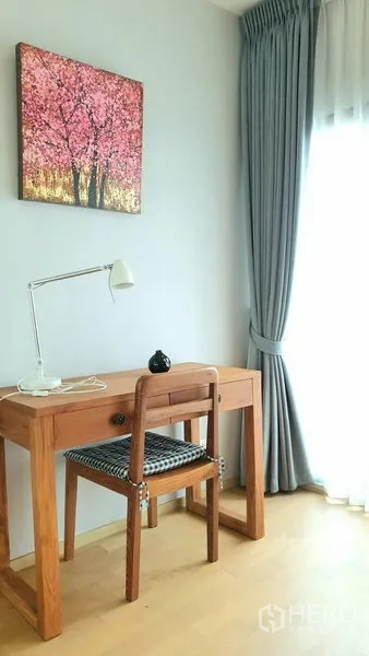 Condominium for rent or sale in Watthana, Bangkok - Quiet study nook with wooden desk and chair by a window with curtains.