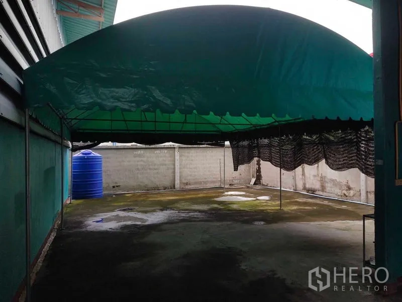 货栈 出售在Lam Luk Ka, Pathum Thani - 户外遮阳棚区域，绿色篷顶与蓝色水塔靠墙