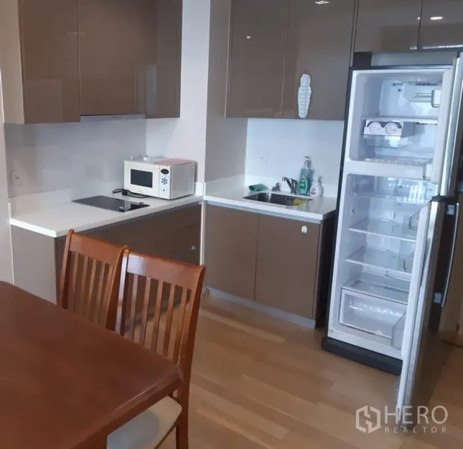 คอนโด ให้เช่าในKhlong Toei, Bangkok - ครัวยุคใหม่ขนาดกะทัดรัด ตู้บิ้วท์อินสีน้ำตาล ท็อปสีขาว เตาไฟฟ้า ไมโครเวฟ อ่างล้างจาน และตู้เย็นแบบสูงเปิดอยู่