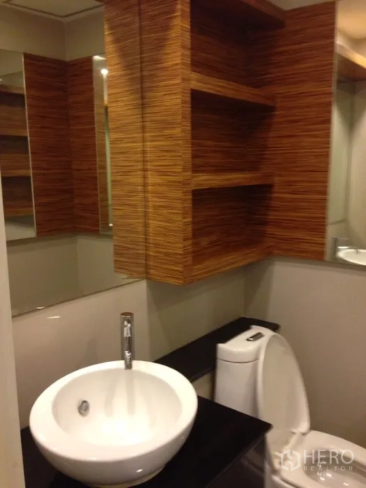 Condominium for rent in Khlong Toei, Bangkok - Compact bathroom featuring vessel sink, wooden open shelves and a toilet.