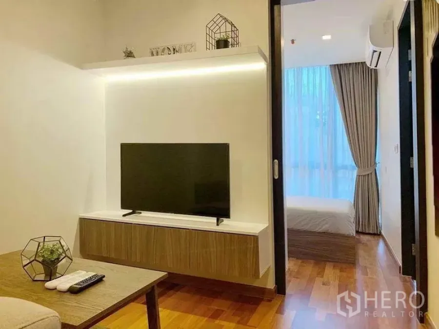 Condominium for sale in Ratchathewi, Bangkok - Living room with floating TV console, wood floors and sliding door to bedroom.