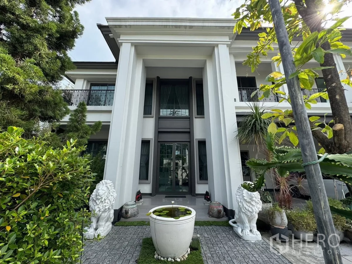 独立式住宅 出售在Mueang Pathum Thani, Pathum Thani - 宏伟门庭，高柱与玻璃门，两侧狮子雕像与庭院水缸。