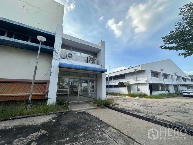 Factory for rent in Khlong Luang, Pathum Thani - Main glass entrance with blue canopy beside factory buildings