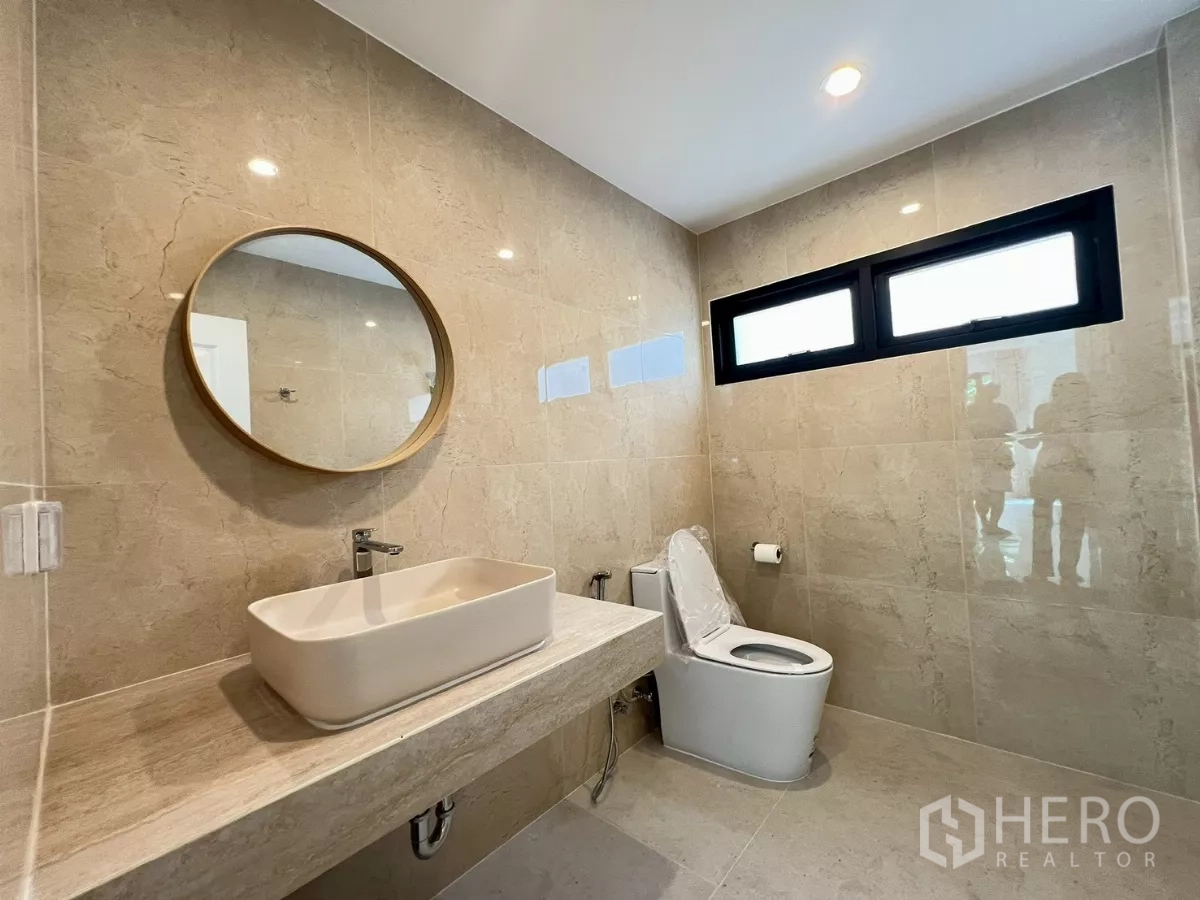 บ้าน ให้เช่าในSuan Luang, Bangkok - ห้องน้ำสไตล์ร่วมสมัย ผนังหินอ่อนโทนเบจ กระจกวงกลม และอ่างล้างหน้าเคาน์เตอร์.