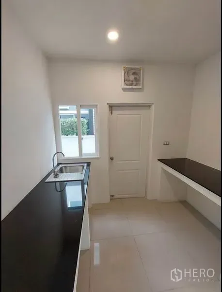 บ้าน ขายในBang Yai, Nonthaburi - ครัวแบบแกลเล่ย์สว่าง เคาน์เตอร์หินสีดำ อ่างล้างจาน หน้าต่าง และประตูหลังบ้าน