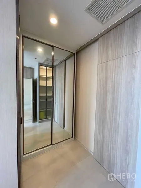Condominium for rent in Pathum Wan, Bangkok - Walk-in corridor with mirrored sliding wardrobe doors and built-in shelving.