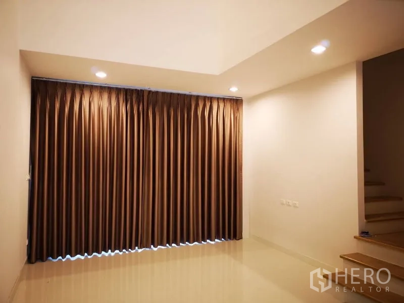 ทาวน์เฮาส์ ให้เช่าในBang Na, Bangkok - ห้องชั้นล่างพร้อมผ้าม่านทึบเต็มผนัง ไฟสปอตไลท์ และทางขึ้นบันได