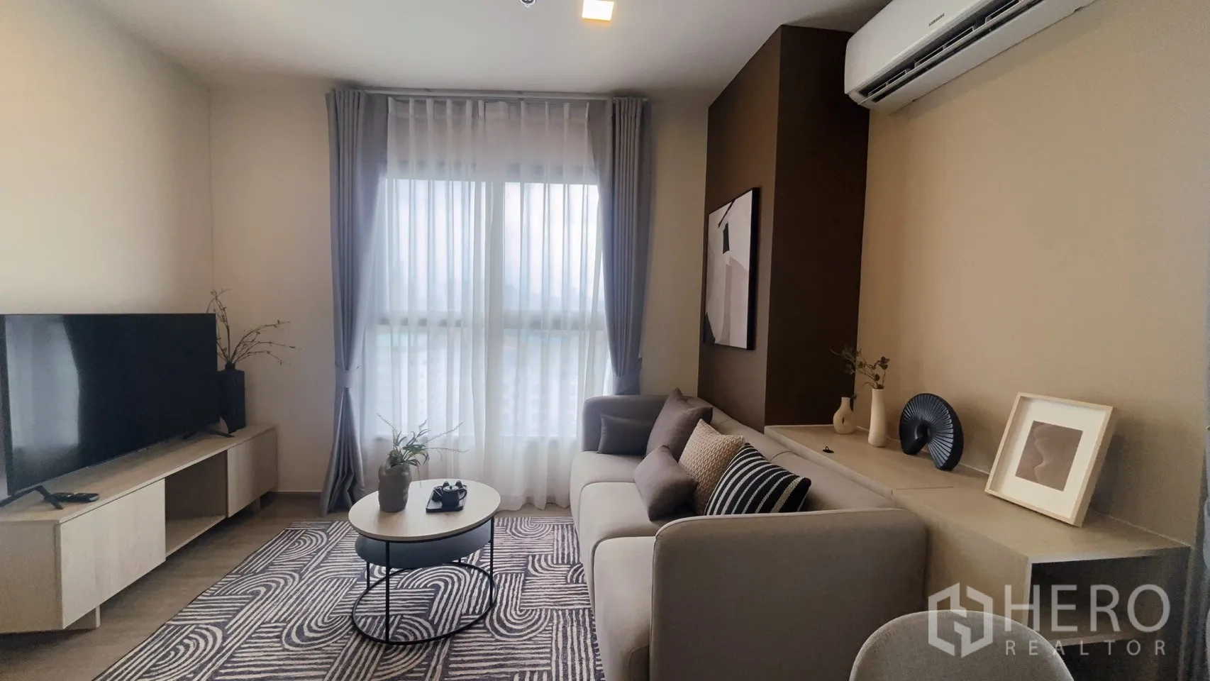 Condominium for rent in Watthana, Bangkok - Cozy living room featuring sofa, round coffee table, TV console, and full-length windows.