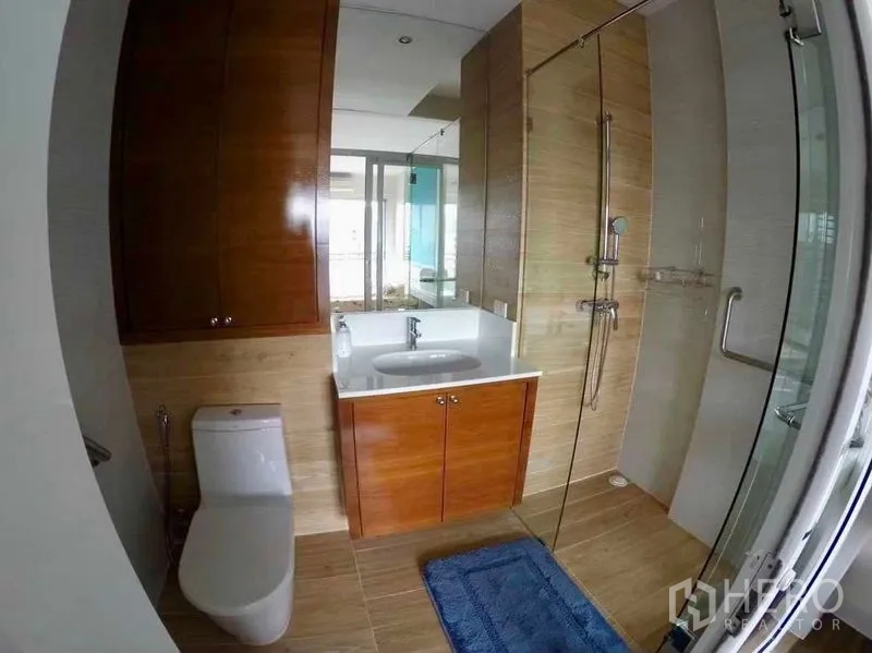 Condominium for rent or sale in Khlong San, Bangkok - Modern bathroom with glass-enclosed shower, wood vanity and tiled walls.