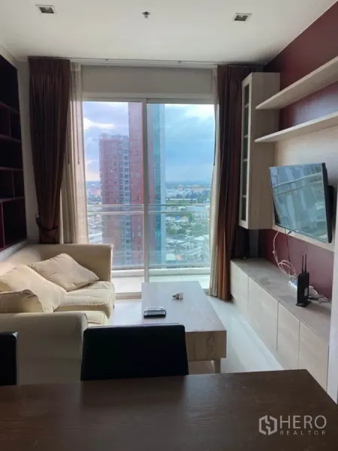 Condominium for rent in Watthana, Bangkok - Bright living room with sofa, TV wall, built-in shelves and floor-to-ceiling window opening to a balcony with city view