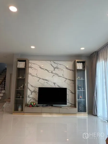 Detached House for rent in Bang Phli, Samut Prakan - TV feature wall with marble-look panel and built-in display cabinets beside sliding glass doors.