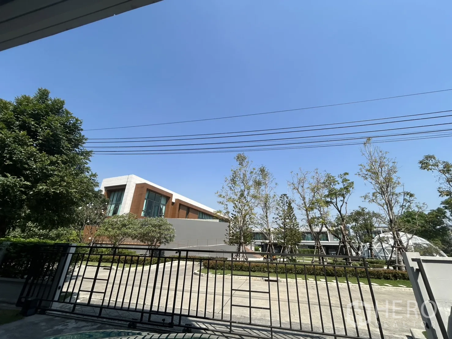 Detached House for rent in Bang Phli, Samut Prakan - View from the front gate toward contemporary community buildings and trees.